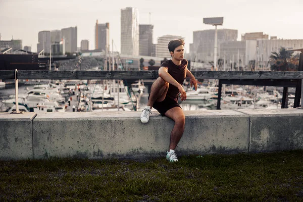 Hombre atlético joven después de correr en el parque con antecedentes rascacielos —  Fotos de Stock