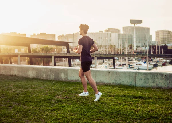 Hombre atlético joven corriendo en el parque con antecedentes de rascacielos —  Fotos de Stock