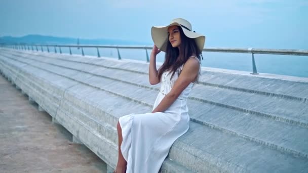 Красива жінка в білій сукні і памела капелюх сидить — стокове відео