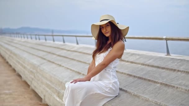 Mujer bonita con vestido blanco y sombrero de pamela sentado — Vídeo de stock