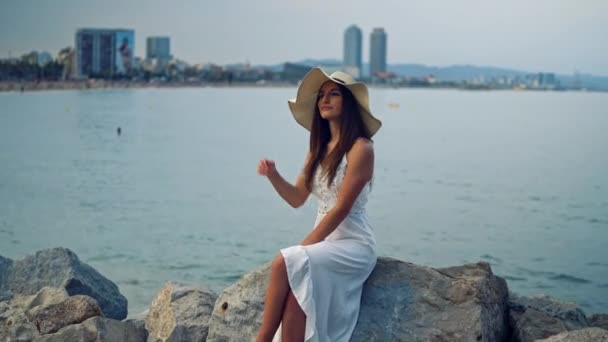Красивая женщина в белом платье и шляпе Памелы сидит — стоковое видео