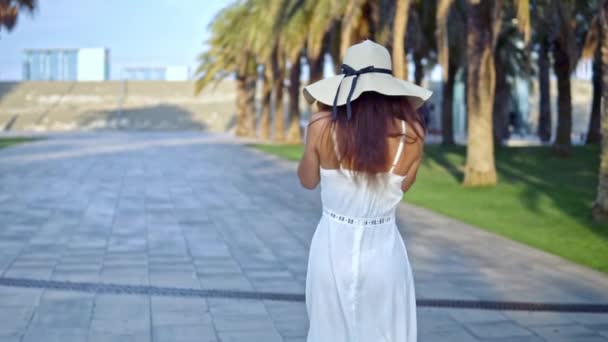 Mujer bonita con vestido blanco y sombrero de pamela caminando — Vídeo de stock