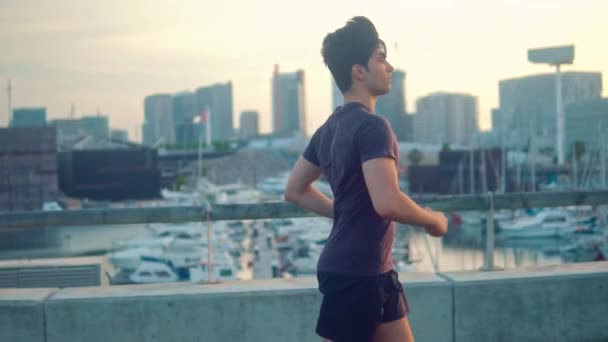 Jeune homme athlétique courir au parc avec des gratte-ciel arrière-plan — Video