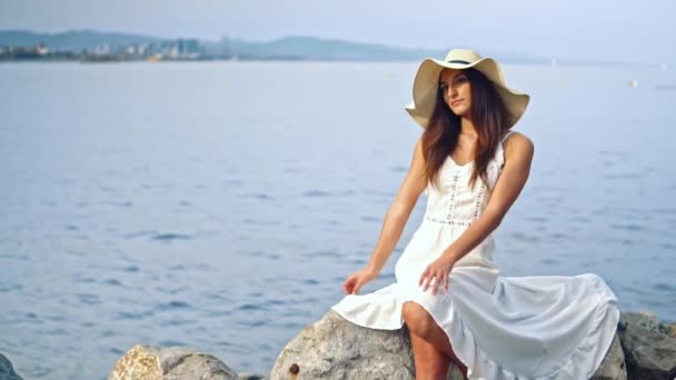 Красива жінка в білій сукні і памела капелюх сидить — стокове відео