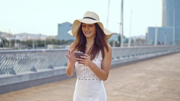 Mujer bonita con vestido blanco y sombrero de pamela caminando — Vídeos de Stock