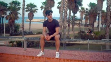 Genç atletik adam plaja yakın palmiye ağacı parkta oturan