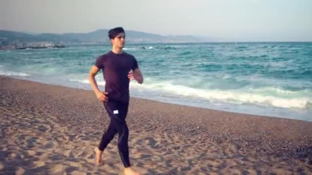 युवा एथलेटिक आदमी समुद्र तट पर दौड़ रहा है। स्वास्थ्य अवधारणा — स्टॉक वीडियो