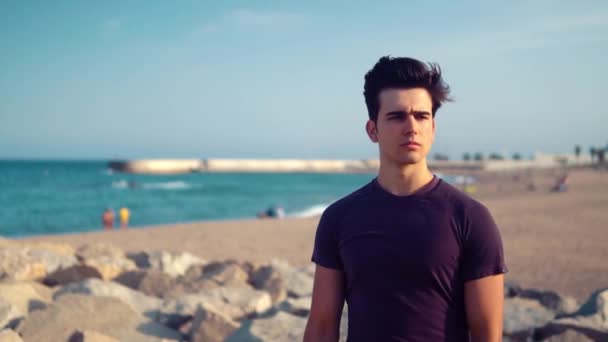 Homem atlético jovem em pé na praia de pedra. Conceito de saúde — Vídeo de Stock