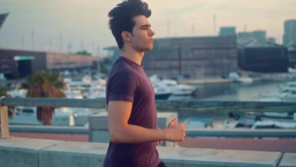 Jeune homme athlétique courir au parc avec des gratte-ciel arrière-plan — Video