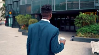 Mavi takım elbise giyen Afro-Amerikan işadamı ofis yakınında kahve içiyor