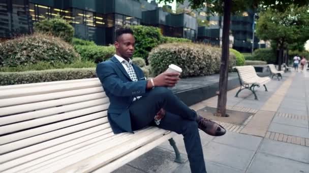 Hombre de negocios afroamericano con traje azul bebe café cerca de la oficina — Vídeos de Stock