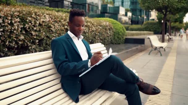 Biznesmen czyta dokumenty lub notebook na sobie niebieski garnitur w pobliżu biura — Wideo stockowe