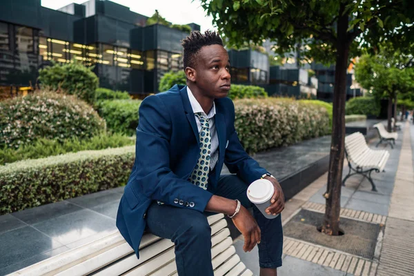 Афроамериканский бизнесмен в синем костюме пьет кофе возле офиса — стоковое фото