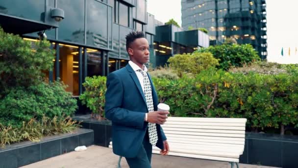 青いスーツを着たアフリカ系アメリカ人のビジネスマンがオフィスの近くでコーヒーを飲む — ストック動画
