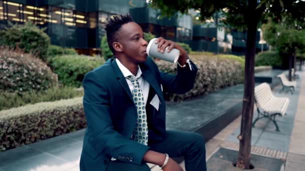 Афроамериканский бизнесмен в синем костюме пьет кофе возле офиса — стоковое видео