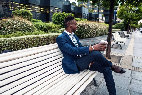 青いスーツを着たアフリカ系アメリカ人のビジネスマンがオフィスの近くでコーヒーを飲む — ストック写真