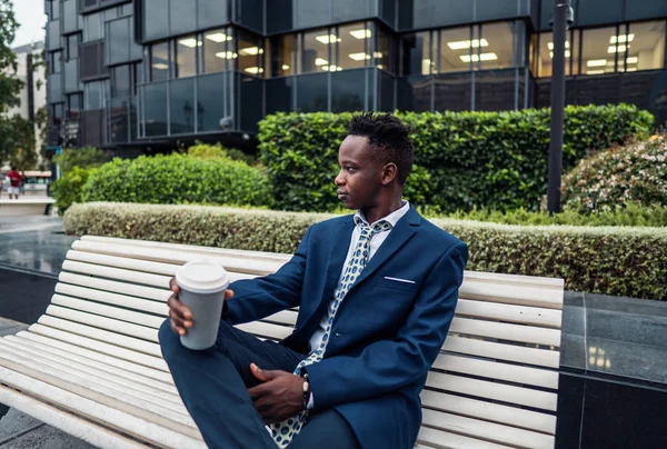 青いスーツを着たアフリカ系アメリカ人のビジネスマンがオフィスの近くでコーヒーを飲む — ストック写真