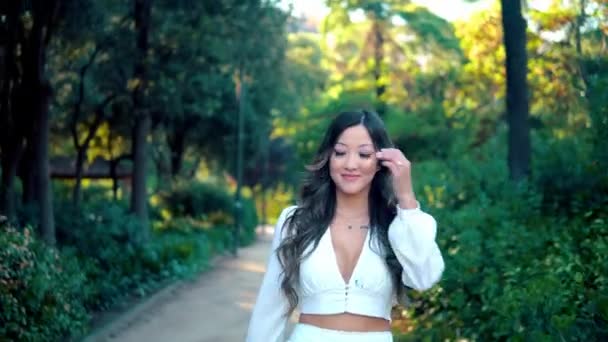 Hermosa chica asiática en vestido blanco sonriendo en el parque — Vídeos de Stock