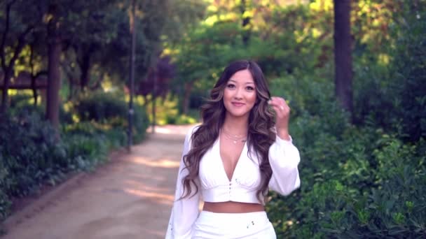 Parkta gülümseyen beyaz elbiseli güzel Asyalı kız — Stok video