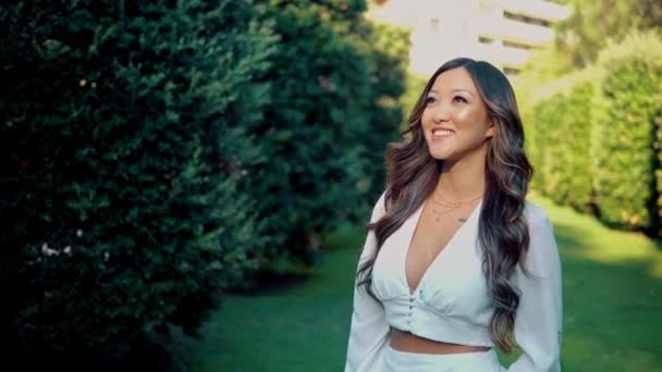 Vacker asiatisk tjej i vit klänning leende i parken — Stockvideo