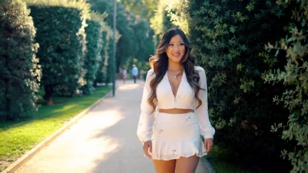 Hermosa chica asiática en vestido blanco sonriendo en el parque — Vídeos de Stock