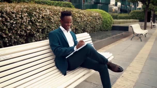 Biznesmen czyta dokumenty lub notebook na sobie niebieski garnitur w pobliżu biura — Wideo stockowe
