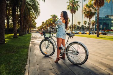 Mavi elbiseli Asyalı model yeşil bir parkta beyaz bir bisiklet sürmek