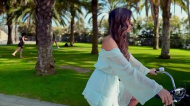 Mavi elbiseli Asyalı model yeşil bir parkta beyaz bir bisiklet sürmek