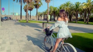 Mavi elbiseli Asyalı model yeşil bir parkta beyaz bir bisiklet sürmek