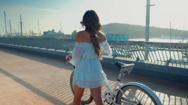 Mavi elbiseli Asyalı model deniz terasında beyaz bir bisiklete biniyor