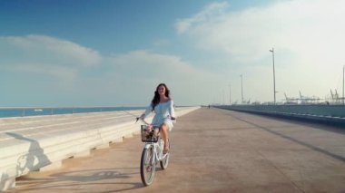 Mavi elbiseli Asyalı model deniz terasında beyaz bir bisiklete biniyor