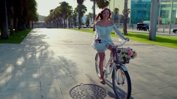 Modelo asiático en un vestido azul monta una bicicleta blanca en un parque verde — Vídeo de stock