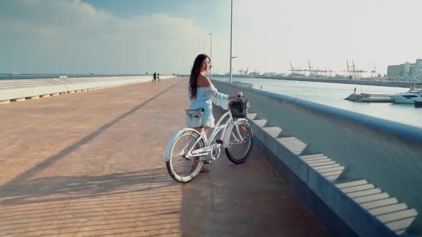 Modelo asiático en un vestido azul monta una bicicleta blanca en la terraza del mar — Vídeo de stock