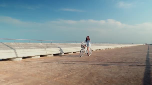 Modelo asiático en un vestido azul monta una bicicleta blanca en la terraza del mar — Vídeo de stock