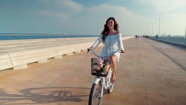 Azjatycki model w niebieskiej sukni jeździ białym rowerem na tarasie morskim — Wideo stockowe