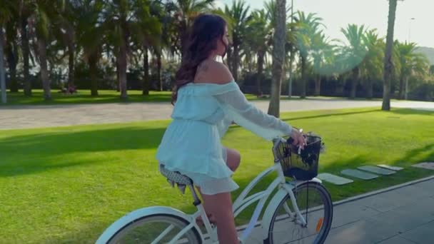 Aziatisch model in een blauwe jurk berijdt een witte fiets in een groen park — Stockvideo