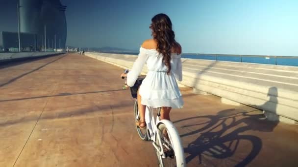 Ασιατικό μοντέλο σε ένα μπλε φόρεμα βόλτες με ένα λευκό ποδήλατο στη βεράντα της θάλασσας — Αρχείο Βίντεο