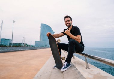 Kaykaycı modern şehir deniz terasında kaykay ile oturur