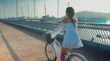 Mavi elbiseli Asyalı model deniz terasında beyaz bir bisiklete biniyor