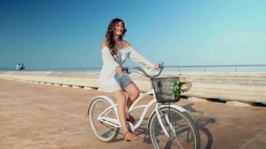 Mavi elbiseli Asyalı model deniz terasında beyaz bir bisiklete biniyor