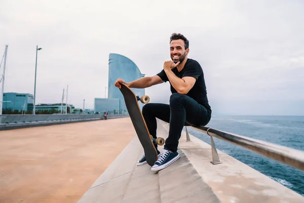 Skateboarder se sienta con monopatín en la moderna terraza del mar de la ciudad — Foto de Stock