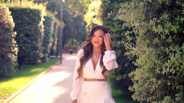 Hermosa chica asiática en vestido blanco sonriendo en el parque — Vídeos de Stock