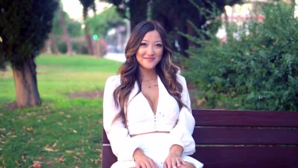 Hermosa chica asiática en vestido blanco sonriendo en el parque — Vídeos de Stock