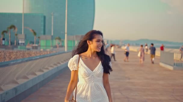 Mooi meisje in de witte jurk wandelen langs de zeepromenade — Stockvideo