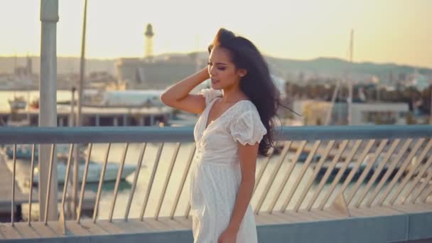 바다 산책로를 따라 걷는 흰색 드레스를 입은 아름다운 소녀 — 비디오