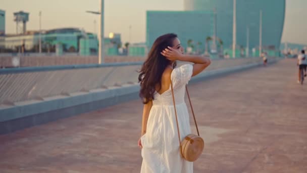Красивая девушка в белом платье прогуливается по морской набережной — стоковое видео