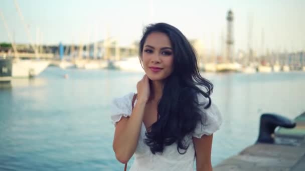 Красивая девушка в белом платье прогуливается по морской набережной — стоковое видео