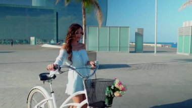 Mavi elbiseli Asyalı model deniz terasında beyaz bir bisiklete biniyor