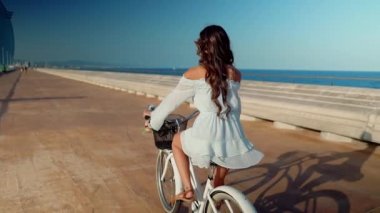 Mavi elbiseli Asyalı model deniz terasında beyaz bir bisiklete biniyor