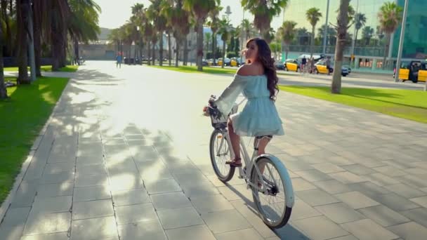 Modelo asiático en un vestido azul monta una bicicleta blanca en un parque verde — Vídeo de stock